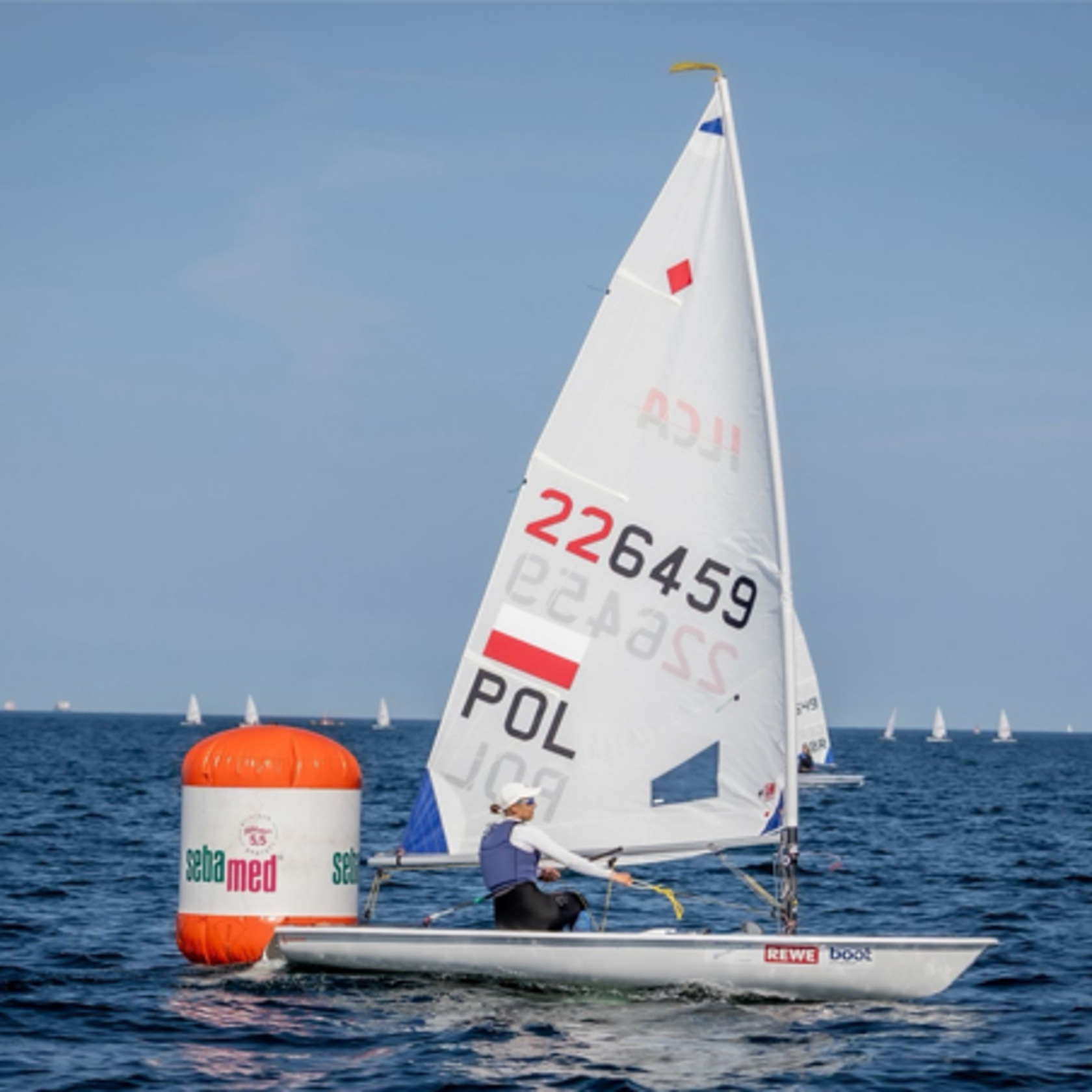Ein Segelboot mit einer Person an Bord auf dem Meer, mit Markierungsboje.