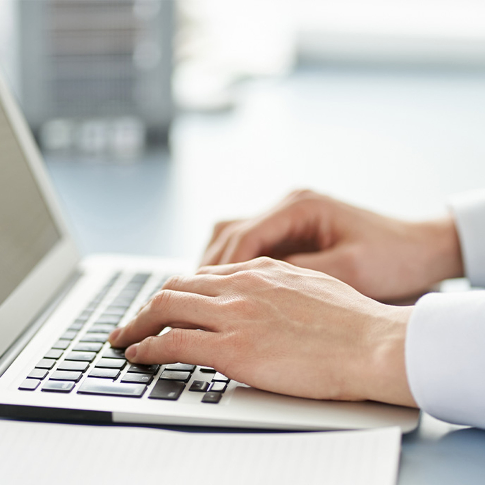 Person tippt auf einer Laptop-Tastatur, Nahaufnahme der Hände.