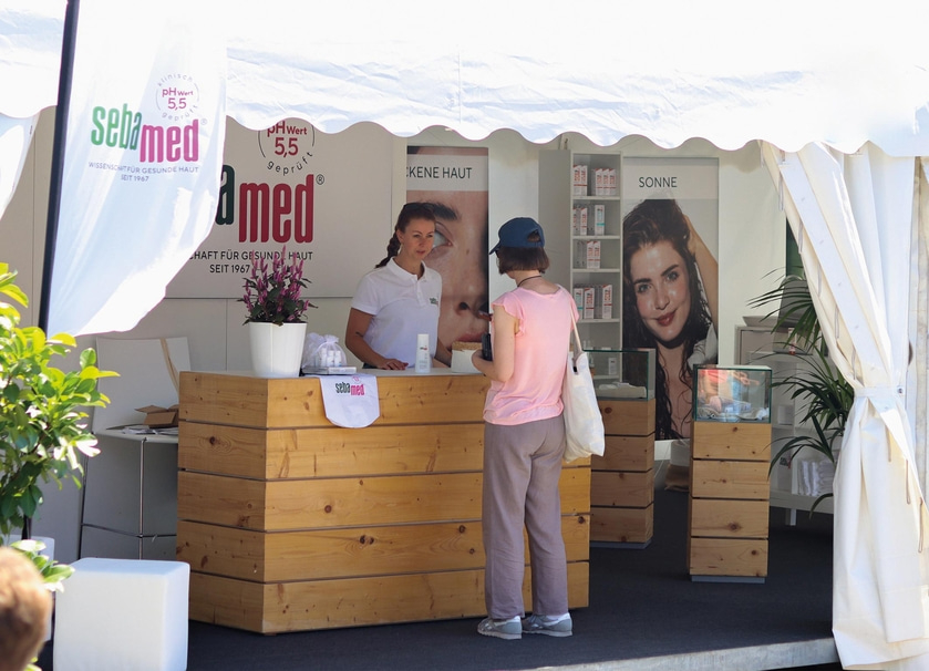 Sebamed-Stand mit Verkäuferin und Kundin, Werbung für Hautpflegeprodukte.