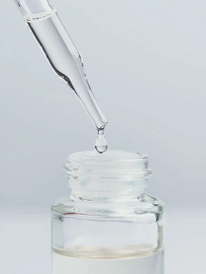 Tropfen fallen aus einer Pipette in eine Glasflasche mit Flüssigkeit.