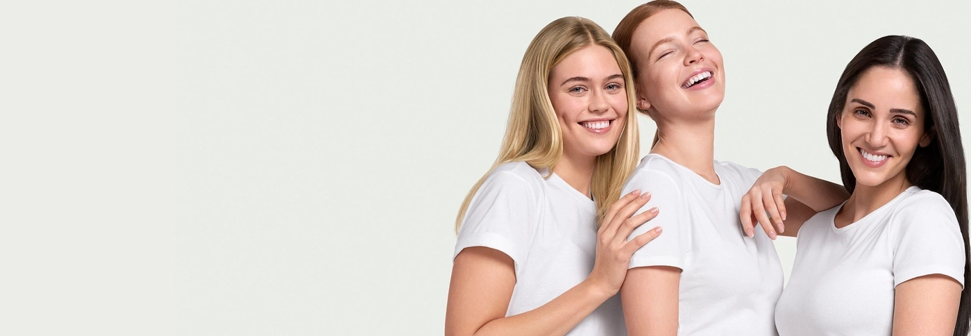 Drei lächelnde Frauen in weißen T-Shirts, die sich umarmen und Spaß haben.