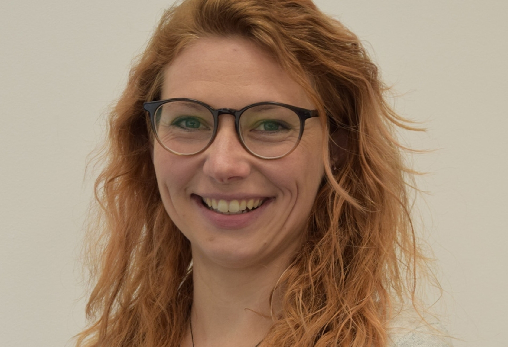 Eine lächelnde Frau mit Brille und roten Haaren, die in die Kamera schaut und lächelt.