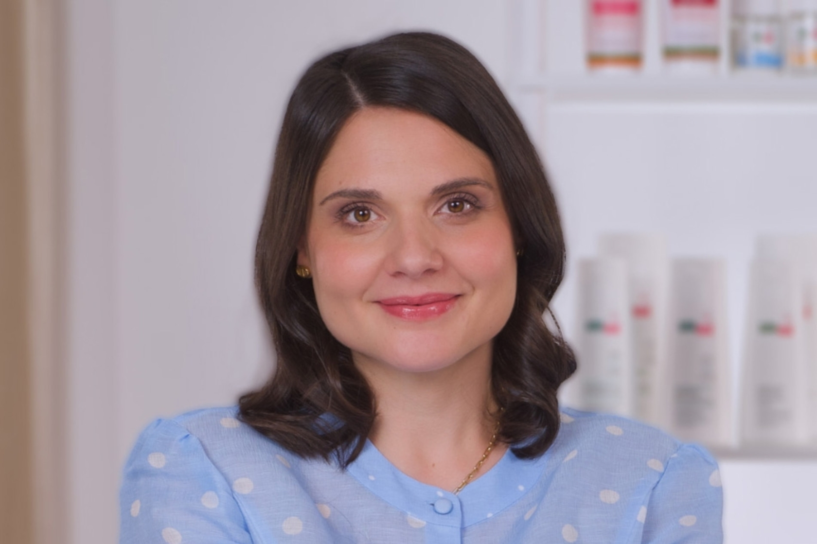 Frau mit braunen Haaren lächelt in blauem Polka-Dot-Hemd.