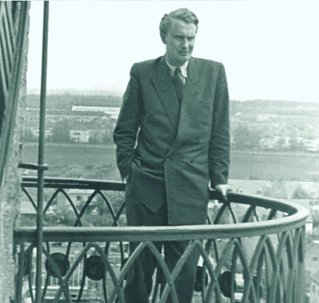 Mann im Anzug steht auf einem Balkon mit Blick auf die Landschaft.