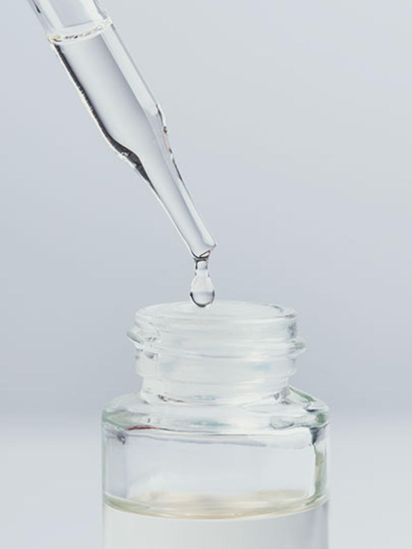 Tropfen fallen aus einer Pipette in eine Glasflasche mit Flüssigkeit.