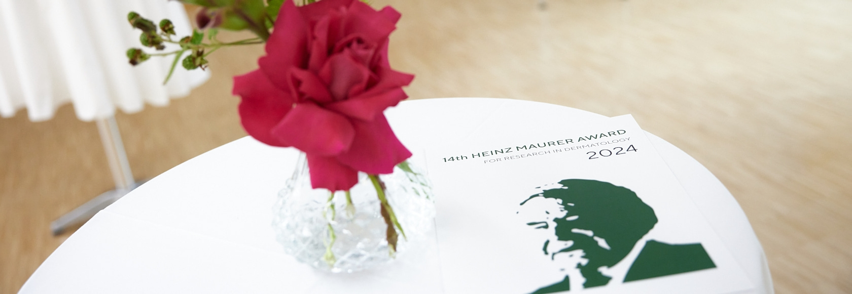 Nahaufnahme einer roten Rose in einer Vase neben einer Auszeichnung für Dermatologie.