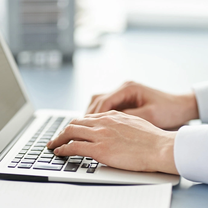 Person tippt auf einer Laptop-Tastatur, Nahaufnahme der Hände.