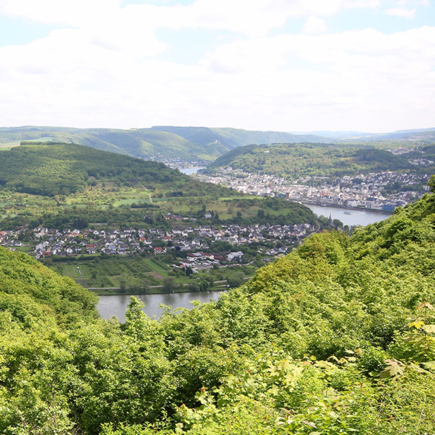 Landschaft mit Hügeln, Stadt und Fluss unter blauem Himmel mit Wolken