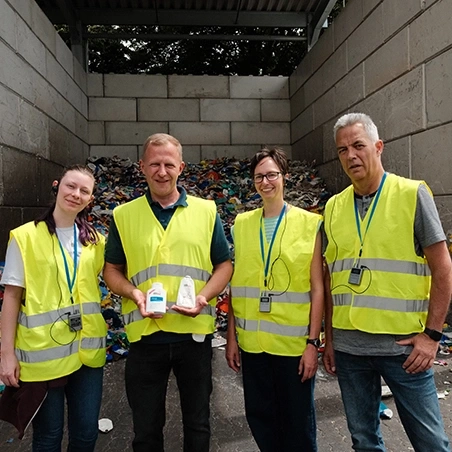 Vier Personen in Warnwesten halten Flaschen in einer Recyclinganlage.