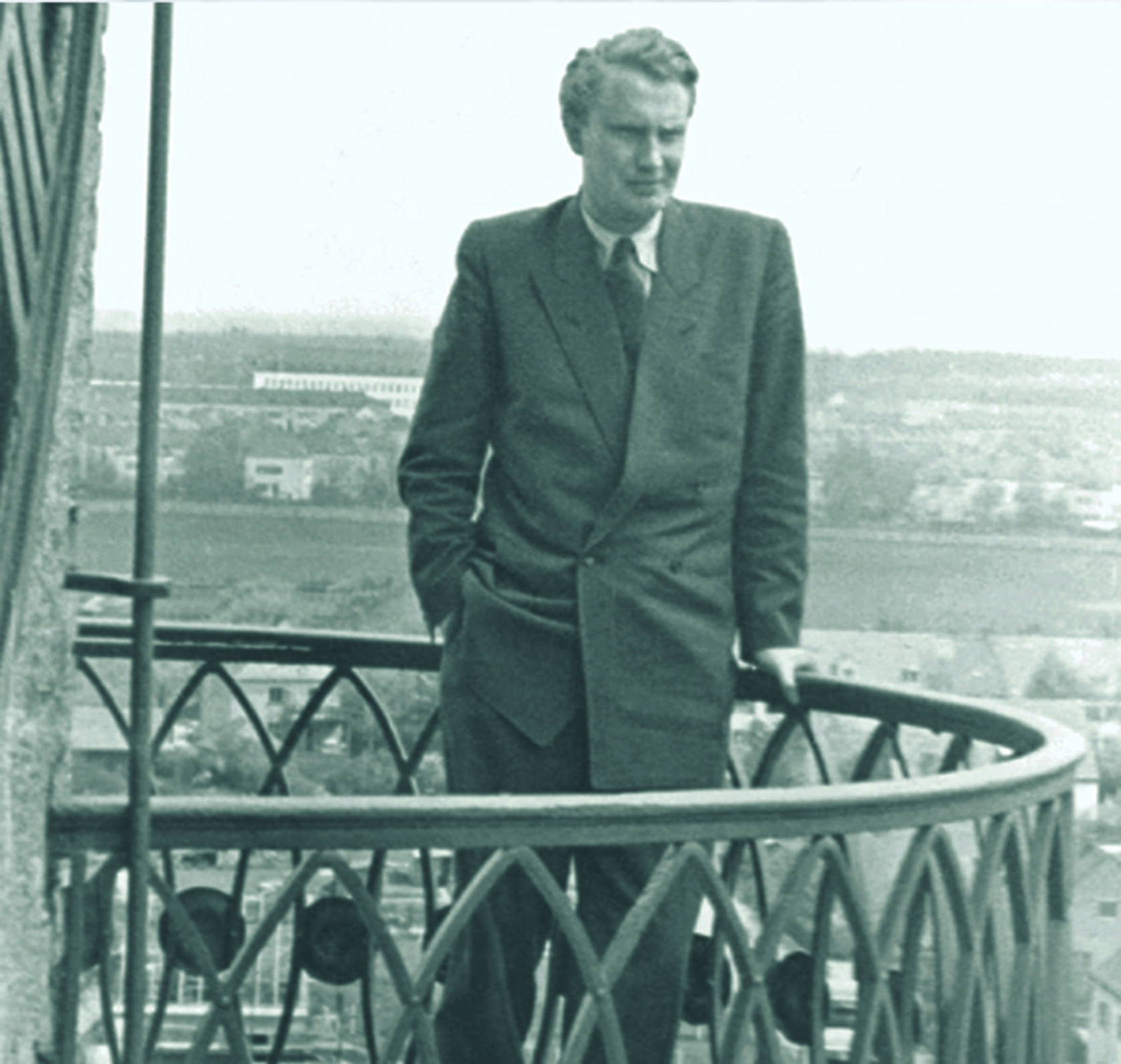 Mann im Anzug steht auf einem Balkon mit Blick auf die Landschaft.