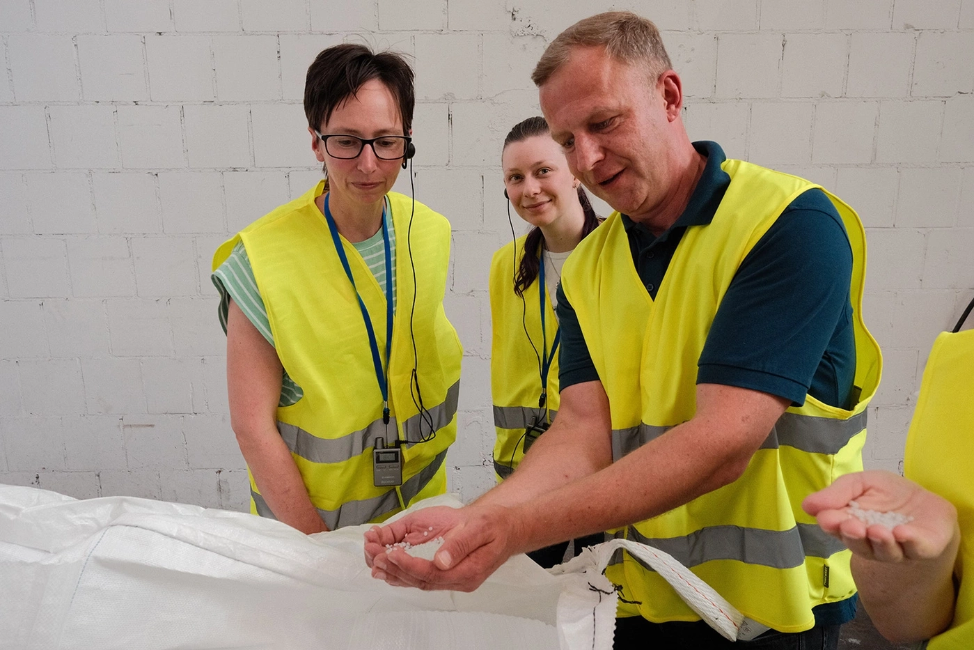 Mitarbeiter in Warnwesten zeigen Plastikgranulat im Lager.