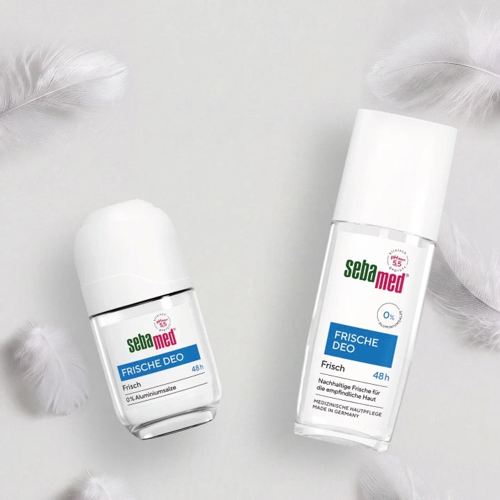 Zwei Sebamed Deo-Flaschen, eine Roll-On und eine Sprühflasche, mit Federn auf weißem Hintergrund.
