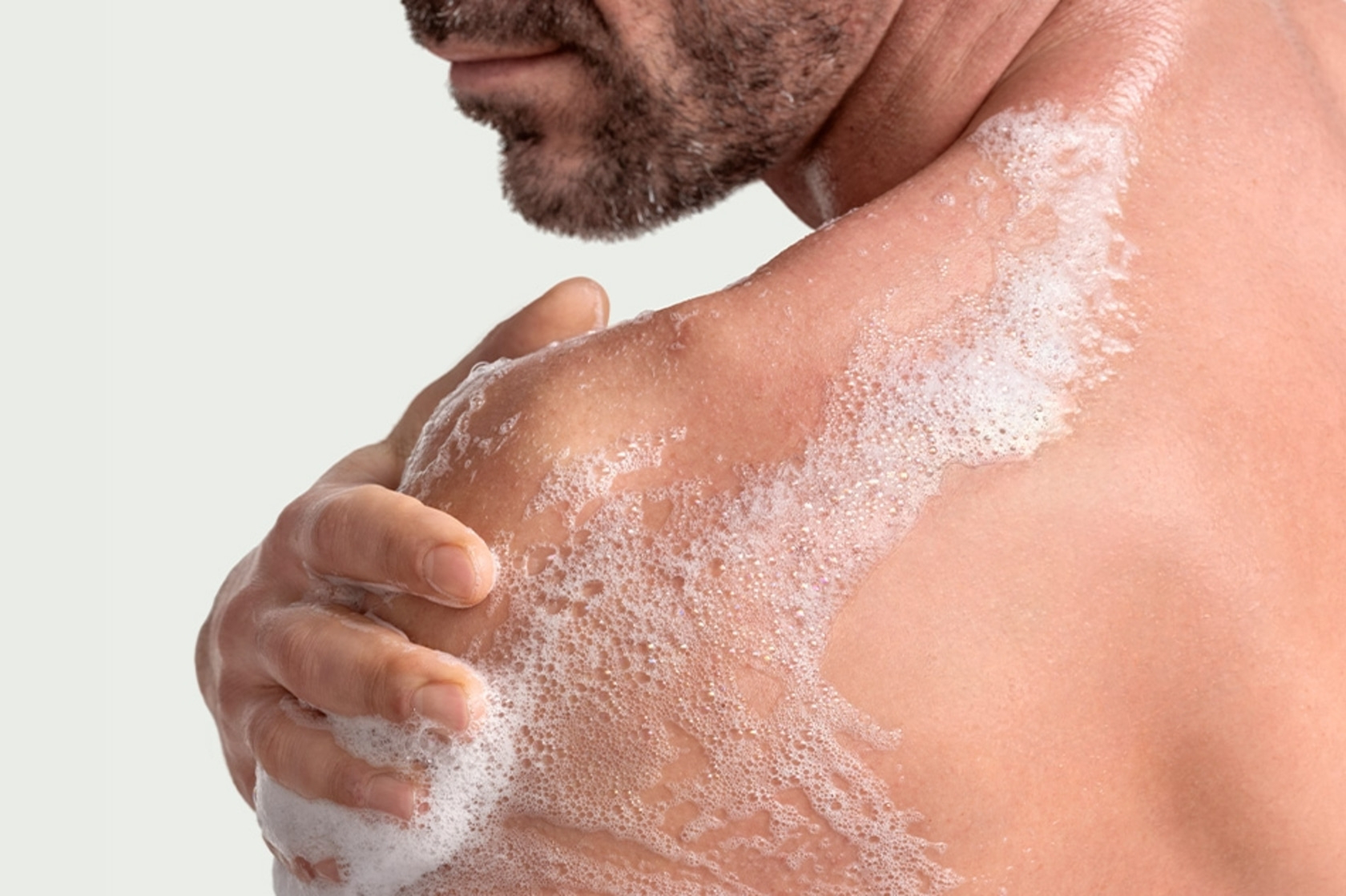 Mann wäscht sich mit Seife unter der Dusche, Schaum auf der Haut