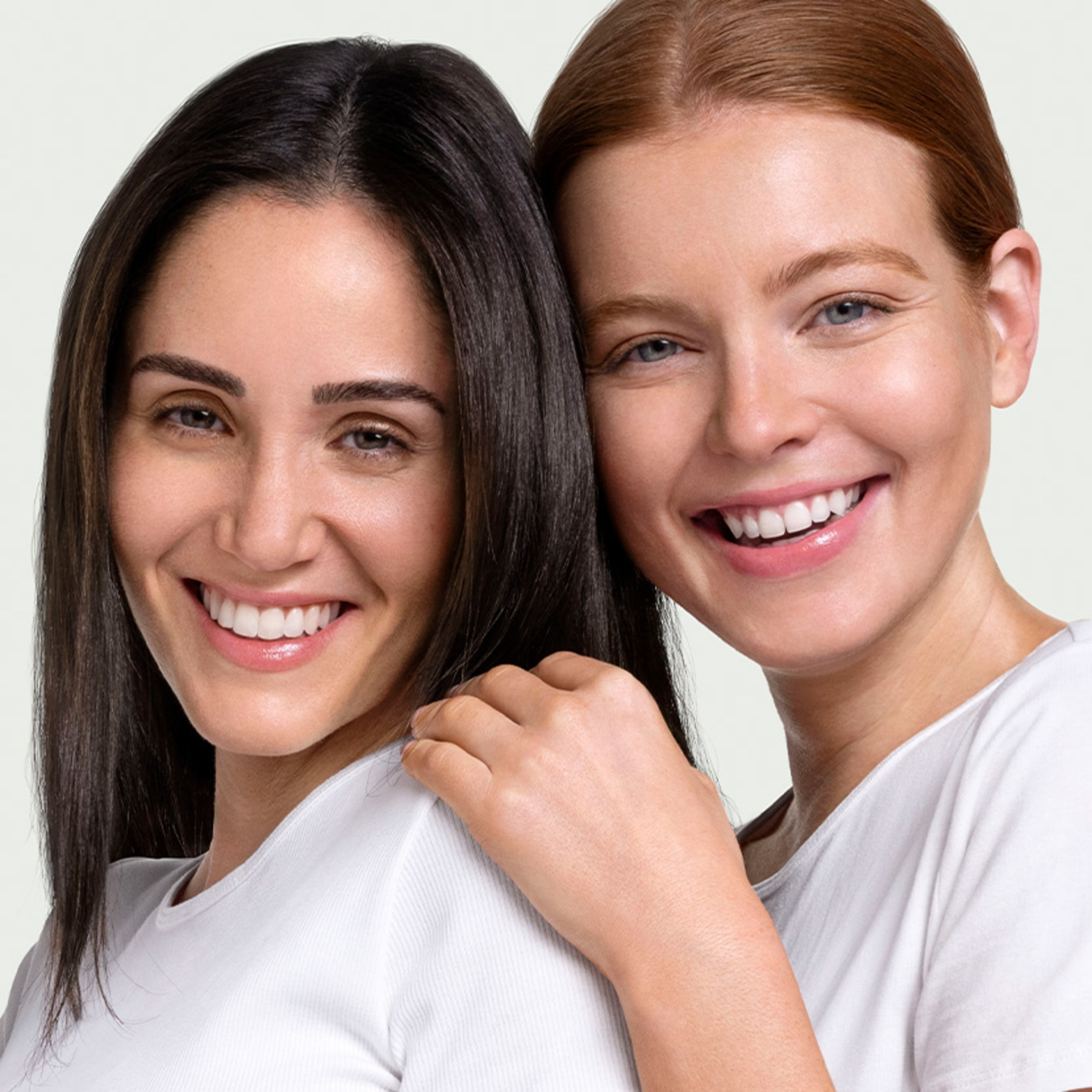 Zwei lächelnde Frauen in weißen T-Shirts, die sich umarmen und lächeln.