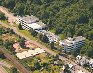 Luftaufnahme eines Gebäudekomplexes mit Bäumen und einer Straße daneben.